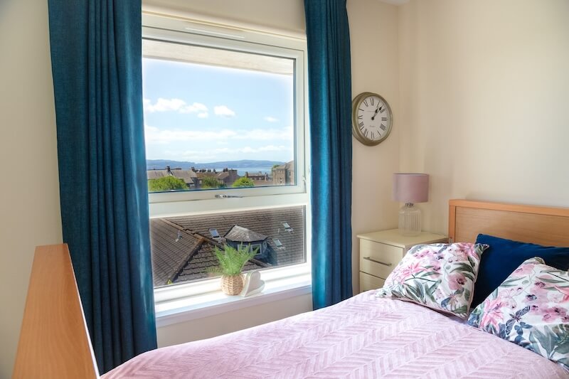 A window with dark blue curtains, a plant on the windowsill, and a bed with pink bedding.