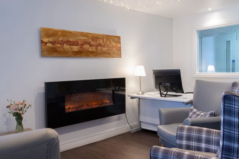 A room view featuring a checkered armchair and an electric fireplace.