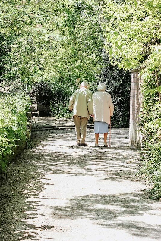 An elderly couple walking in a park, holding hands.