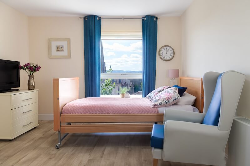 A window with dark blue curtains, a plant on the windowsill, and a bed with pink bedding.