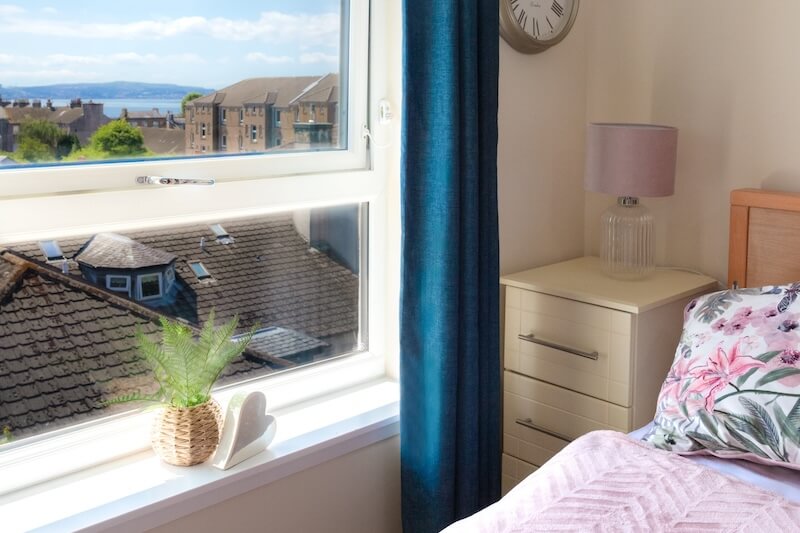 A window with dark blue curtains, a plant on the windowsill, and a bed with pink bedding.