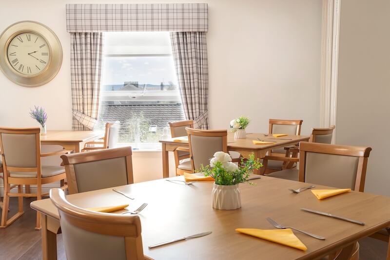 A dining table with checkered curtains at the window.