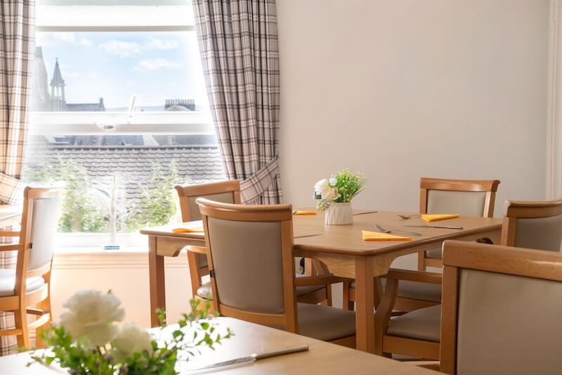 A dining table with checkered curtains at the window.