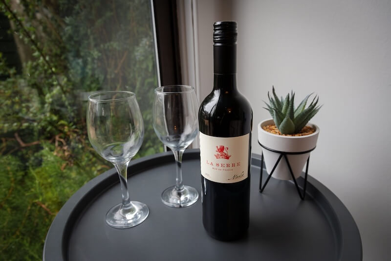 A bottle of red wine and two wine glasses on a table.